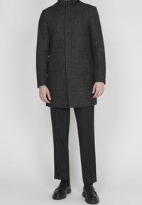 Dopasowany szary płaszcz w jodełkę z wysokim kołnierzem, zapinany na jeden guzik, z długimi rękawami, zestawiony z czarnymi spodniami wizytowymi i butami.