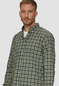 Zielona i kremowa koszula z guzikami w kratkę z kołnierzykiem, z małymi niebieskimi akcentami i miękką teksturą materiału.