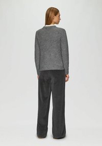 Grauer gerippter Pullover, runder Ausschnitt, lange Ärmel. Kombiniert mit dunkelgrauen, weit geschnittenen Hosen, weiche Textur, leichter Glanz.