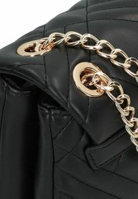 Borsa a tracolla in pelle trapuntata nera con catena dorata, caratterizzata da occhielli metallici rotondi e una texture liscia. Dettagli di cucitura notevoli.