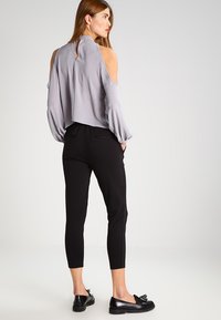 Sivá blúzka s odkrytými plecami a voľnými rukávmi, doplnená o čierne prispôsobené nohavice a čierne mokasíny. Hladká látka a pohodlný strih.