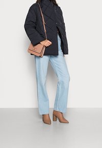 Zwarte doorgestikte jas met drukknoopsluitingen, lichtblauwe wijde jeans en beige enkellaarsjes met blokhak. Heeft een beige crossbodytas.