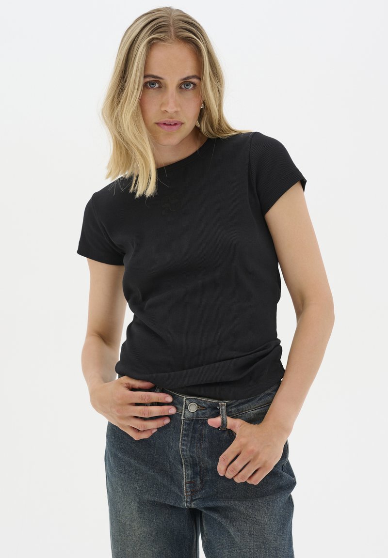 Svart ribbad t-shirt med korta ärmar, rund halsringning och diskret logodetalj. Kombinerad med högmidjade denimjeans.