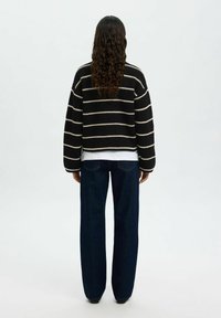 Maglione a strisce nero e crema, corto, a maglia, con maniche lunghe, abbinato a jeans in denim scuri e larghi. Design pulito e minimalista.