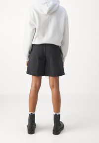 Tmavě džínové šortky s volným střihem, středním pasem a bočními kapsami. Kombinovány s světle šedou mikinou s kapucí a černými kotníkovými botami.