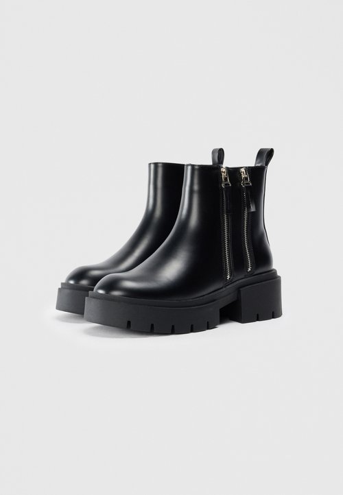 Bottines noires en cuir brillant avec une semelle épaisse noire et des fermetures éclair sur les côtés. Dotées de tirants pour un enfilage facile.