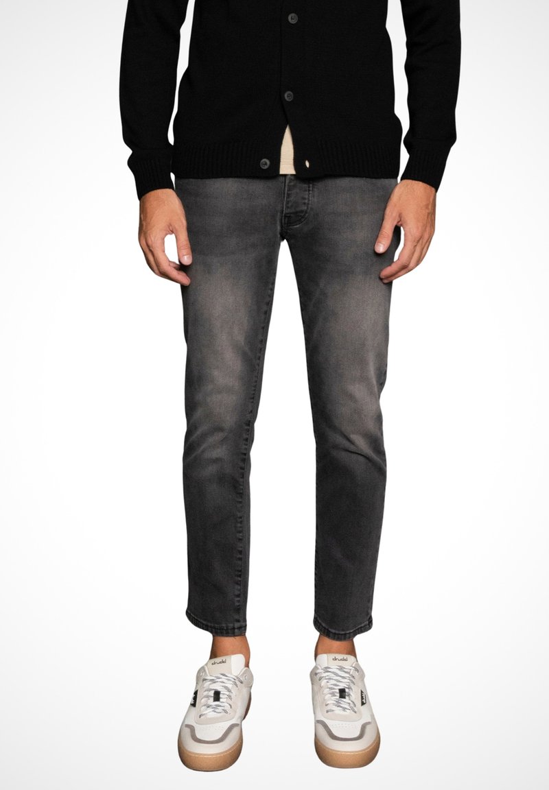 Cardigan negro con botones, combinado con jeans ajustados de corte slim en gris desvanecido. El calzado son zapatillas blancas con una suela texturada en gris y acentos sutiles.