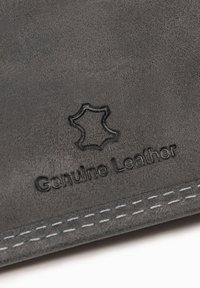 Superficie de cuero genuino marrón oscuro con símbolo de cuero en relieve y doble costura blanca en el borde.