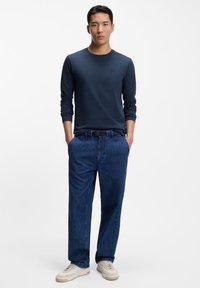 Marineblaues Langarm-T-Shirt mit Rundhalsausschnitt, kombiniert mit blauen Denim-Jeans. Sneakers sind beige mit weißen Details. Einfacher, lässiger Look.