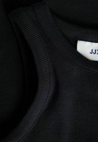 Svart ribbestrikket singlet med rund hals og kontrasterende glatte kanter. Merke synlig med "JJX" i blå skrift.
