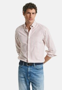 Witte blouse met dunne rode strepen, lange mouwen opgerold tot de ellebogen, gecombineerd met blauwe jeans en een donkere riem.