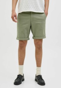 Olive green cotton shorts with turned-up hems, worn with black shoes and cream socks, paired with a textured white top.