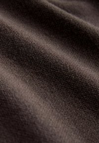 Close-up van bruine stof, met een zachte textuur en een glad, licht donzige oppervlakte, waarop subtiele kleur- en schaduwnuances te zien zijn.