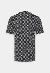 Mustat t-paidat, jossa on koko pinnan kattava toistuva kuvio valkoisista "K"-kirjaimista ja logodesignista eri kokoisina. Lyhyet hihat ja pyöreä pääntie.