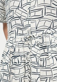 Λευκό φόρεμα με αφηρημένο μαύρο σχέδιο γραμμών, κοντά μανίκια, κουμπωτό μπροστινό μέρος και ζώνη μέσης που δένεται.