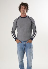 Grijze gebreide trui met marineblauwe accenten en witte strepen op de mouwen, gecombineerd met lichtblauwe jeans. Glad textuur en slim fit ontwerp.