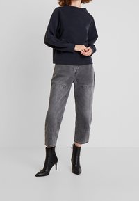 Felpa corta di colore blu navy scuro con colletto rotondo, abbinata a jeans tapered grigi a vita alta con tasche laterali, e stivaletti neri con punta a stiletto.