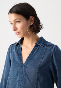 Denimskjorte med dyp V-hals, med et strukturert chevronmønster langs knappefellen, mykt stoff og lette pufferm.