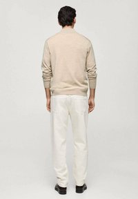 Beige knit sweater with ribbed cuffs, paired with white straight-leg pants. Minimalist design, back view shows smooth texture and no patterns.