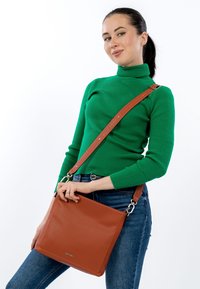 Brūna ādas soma ar pāri pār plecu, ar strukturētu dizainu, izceltām šuvēm un plata siksna. Virsma ir graudaina.