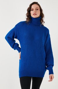 Koninklijk blauwe coltrui met een losse pasvorm, geribbelde manchetten en zoom. Zachte textuur met een gezellige uitstraling en lange mouwen.
