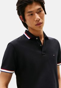 Polo negro de manga corta, con cuello acanalado de rayas de colores y pequeño logo en el pecho. Tejido de mezcla de algodón.