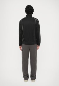 Chaqueta negra con cremallera y ribetes blancos, combinada con pantalones de chándal grises de corte holgado. Tejido suave con puños y cintura acanalados.