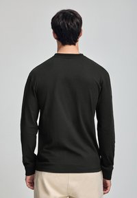 Svart långärmad tröja med rund halsringning, tillverkad av mjukt tyg. Har åtsittande ärmslut och en jämn textur, sedd bakifrån.