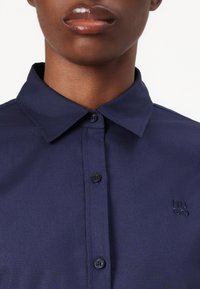 Camicia col colletto blu marina con finitura testurizzata, dotata di due bottoni neri e discreto logo ricamato "HUGO" sul petto.