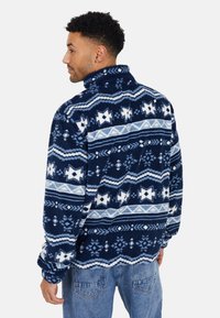 Pullover in pile navy con motivi geometrici bianchi e blu chiaro, colletto alto e polsini elastici. Tessuto morbido e con texture.