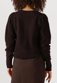 Donkerbruine gebreide trui met puffed mouwen, geribbelde textuur en een ronde halslijn, gecombineerd met een effen bruine rok.