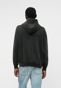 Sweatshirt à capuche noire avec une texture douce et une coupe décontractée. Présente un détail de couture sur le dos et des poignets et un ourlet côtelés.