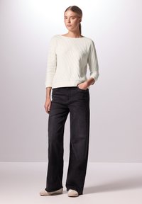 Maglione grigio chiaro con trama, con scollo a giro, abbinato a jeans neri a gamba larga con vita alta. Design semplice, stile casual e tessuto morbido.