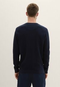 Navyblauwe gebreide trui met lange mouwen, ronde halslijn en ribgebreide manchetten. Glad oppervlak, minimale details en een standaard pasvorm.