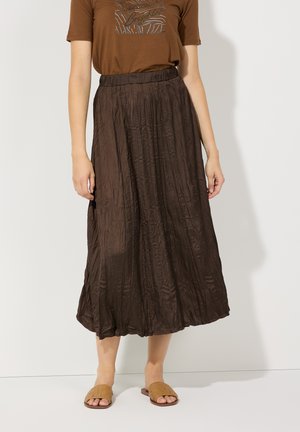 Brown pleated maxi skirt with an elastic waistband and a smooth, shiny texture, paired with beige woven slip-on sandals.