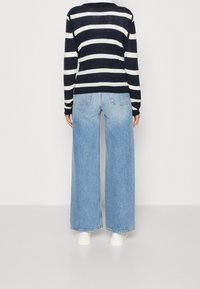 Maglione a righe blu navy e bianche abbinato a jeans a gamba larga blu chiaro, con tasche posteriori e sneakers bianche.