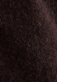 Tissu marron foncé avec une texture douce et duveteuse. Des fibres visibles et un tissage légèrement irrégulier lui confèrent une apparence chaleureuse et confortable.