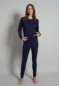 Completo di maglietta a maniche lunghe e leggings di colore blu navy, realizzato in materiale morbido con un motivo ondulato di tonalità più chiara. Caratterizzato da una vestibilità aderente e vita elastica.