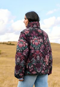 Gesteppte Steppjacke in Schwarz mit floralem Muster in Lila, Grün und Pink. Hoher Kragen und gepolsterte Schultern. Strukturierter Stoff.