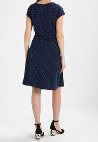 Marinblå klänning med små vita och röda prickar, korta ärmar och en utsvängd kjol. Bärs med svarta klacksandaler med prickigt mönster.