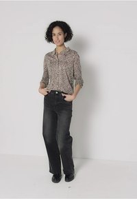 Leopard print button-up shirt with rolled sleeves, paired with high-waisted black jeans. Model stands with hands in pockets, wearing black boots.