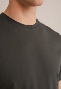 Camiseta de manga corta en gris oscuro, confeccionada en una tela suave. Presenta un escote redondo y una textura lisa, con un detalle de costura mínima.