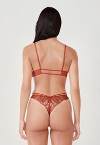 Roestkleurig lingeriesetje met een bralette met slanke bandjes en haakdetails, gecombineerd met een kanten string die fijne bloemmotieven toont.