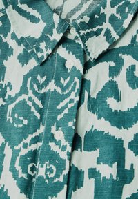 Camicia a maniche corte teal e bianca con un design a pattern. Presenta un colletto classico e chiusure a bottoni bianche lungo la placket.