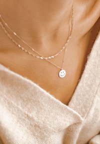 Collane a strati in argento con pendente a forma di faccina sorridente su un colletto texture, con catene delicate e una luminosità sottile.