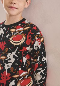 Sort langærmet skjorte med farverigt rensdyrmønster i røde, hvide og brune nuancer, fremhævet af juletemaer og festlige grafik.