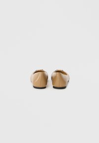 Ballerine in pelle color cammello con forma arrotondata, piccoli dettagli neri e una superficie liscia, caratterizzate da un tacco basso e un design minimalista.