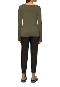 Olivgrünes Langarmoberteil mit rundem Ausschnitt, figurbetontem Schnitt und weicher Textur, kombiniert mit schwarzen, schmal zulaufenden Hosen und Stiefeletten.
