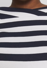 Topp i bomull med horisontella randiga mönster i marinblått och vitt, med en vid hals och en mjuk, elastisk textur. Inga märkbara mönster eller detaljer.