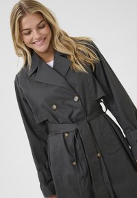 Cappotto trench grigio doppiopetto con vita cinturata, maniche lunghe e tasche a pattina. Realizzato in tessuto liscio e leggero.